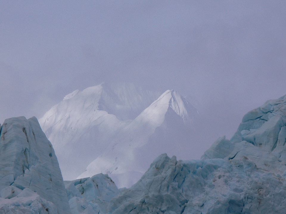Mountains rise through the clouds above a glacier