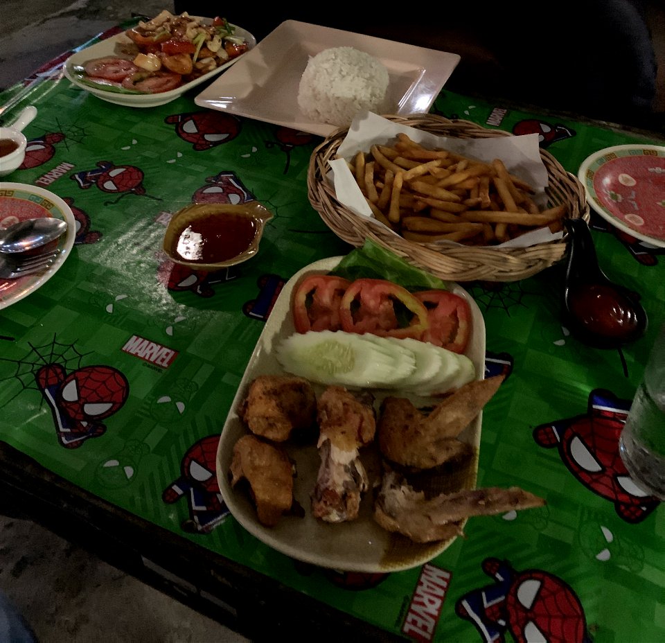 This is a mix of traditional thai foods and western kitchen. Thai Chicken with fish souse, salad, carrots and cashew nuts. With a side order of chicken wings, chips with cucumber and tomato. Served in a traditional thai street restaurant. photo