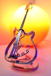 Wire sculpture of an electric guitar in front of a red and yellow globe lamp photo
