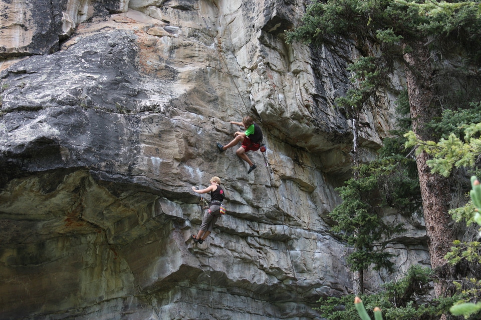 Young man climbs on a rocky wall in a valley with mountains
