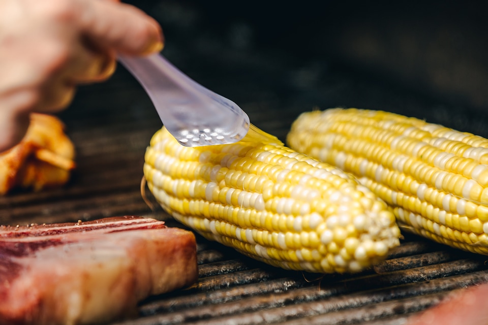 Closeup of a brush applying cooking oil to bbq corn