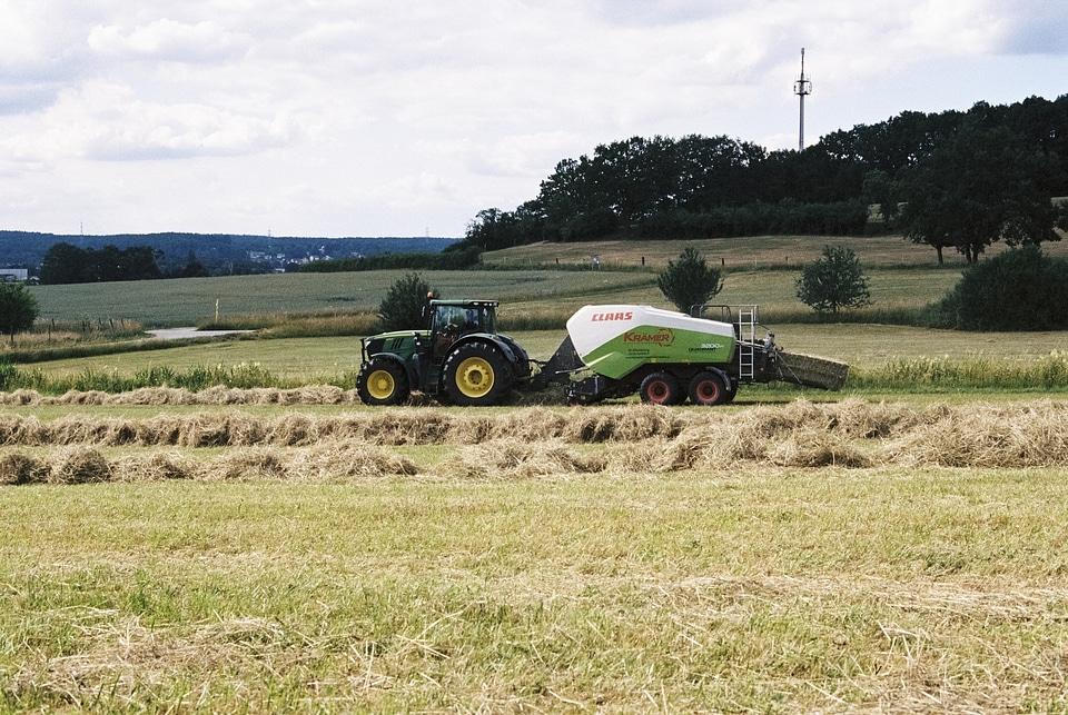 Farmers harvesting hay by tractores in sunny day.
