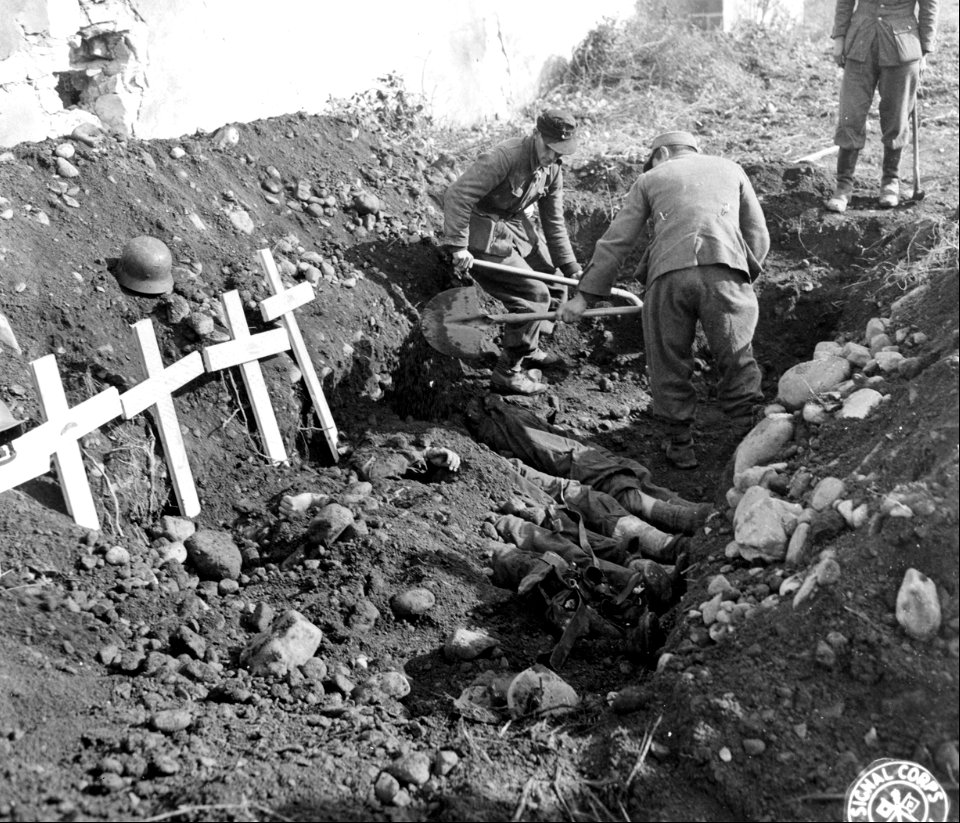 SC 195727 - German prisoners throwing dirt on Nazis interred in common grave. 28 September, 1944.