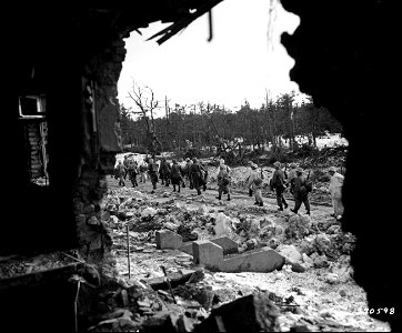 SC 270598 - A contingent of American infantrymen of Co. C, 1st Battalion, 23rd Infantry Regiment, 2nd Infantry Division, march past a ruined building as they return into the Monschau Forest, Germany... photo