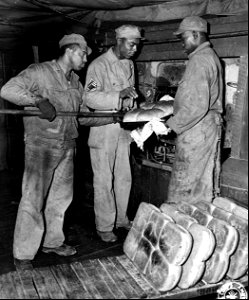 SC 364372 - Three bakers at a depot, somewhere in England, test a fresh pan of loaves as they come out of the oven. photo