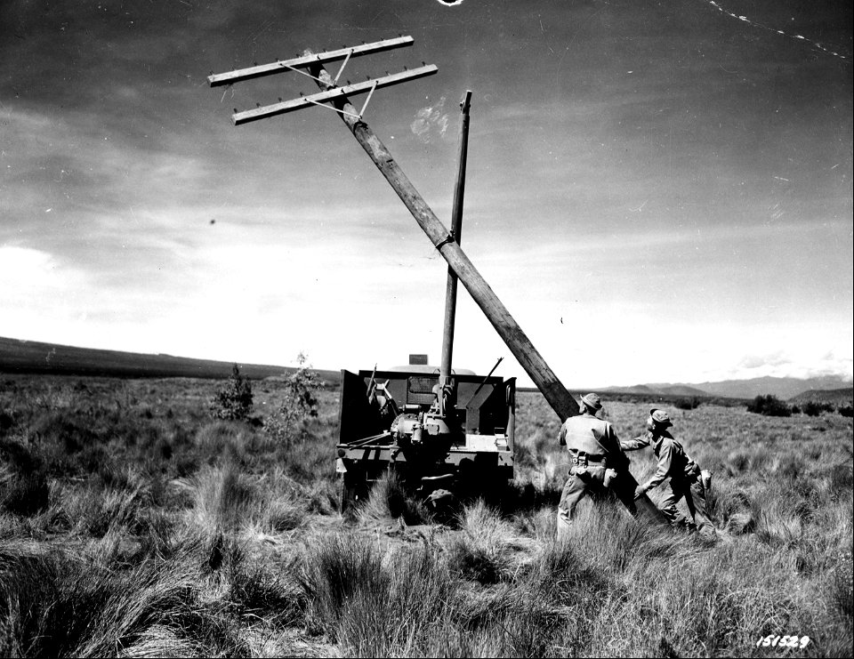 SC 151529 - The earth borer, used for digging post holes, is also used for lifting posts into place. Cpl. John Urban and Pvt. Rex Robinson guide the pole into place. Hawaii.