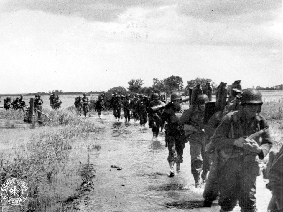 SC 270659 - American troops, real footsloggers, wade through territory in Northern France, flooded by Hitler's forces in an attempt to make glider landing impractical.