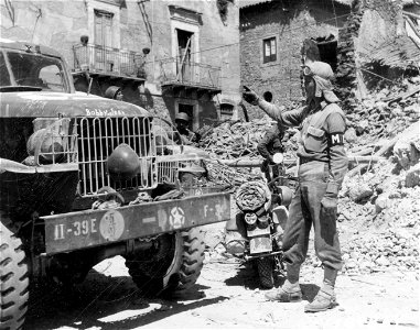 SC 184864 - Pvt. John H. Christopher Abberville, S.C., motorcycle M.P., directs traffic in Barrafranca, Sicily. 19 July, 1943.