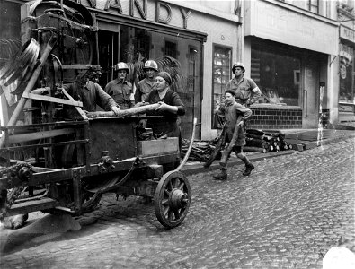 SC 195689 - Three members of a medical unit watch the woodcutting machine at work in the streets of Wiltz, Luxembourg. photo
