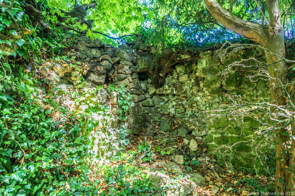 Remains of Boxley Abbey Church. Now a walled garden with a stream running through the middle. Trees growing in the walls.
