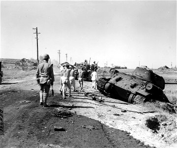 SC 349027 - On their way to a prison camp, POWs are marched past a knocked-out T-34 tank, east of Inchon, Korea. 17 September, 1950.