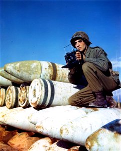 C-769 - Crouching on 16-inch gun shells used in the coastal defense guns at Viareggo, Italy, is Cpl. Marshall Bull, 24, of Oneonta, New York, a still picture photographer with the 196th Signal Photo Company. photo