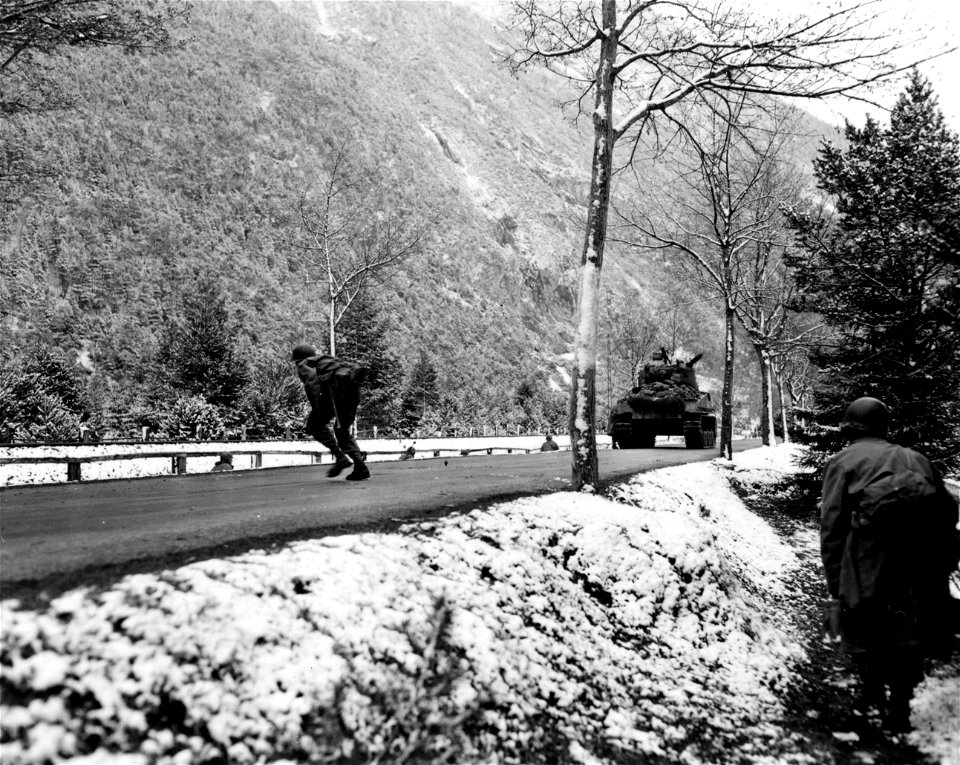 SC 337384 - (409th Task Force photo series) Here, leaving the cover of their ditch, infantry move over road for a better point from which to return fire. 1 May, 1945.