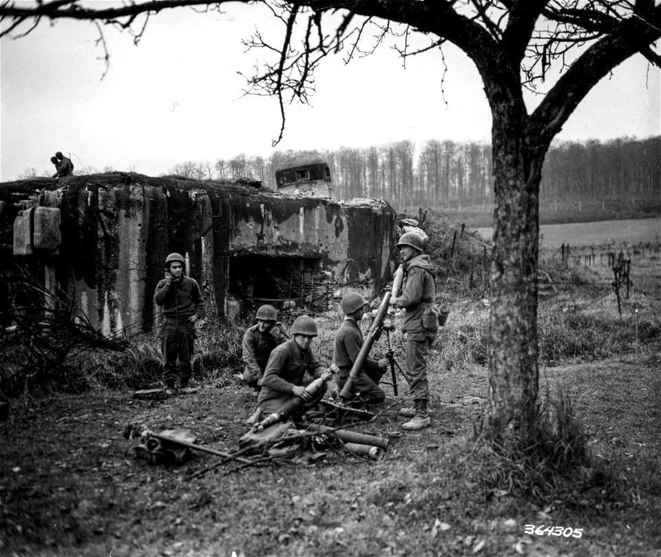 SC 364305 - 45th Division mortar crew, which is sheltered behind the Maginot Line pill-box near Lembach, prepares to fire 81mm shells at enemy.