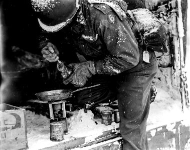 SC 396850 - Wireman heating chow of C rations in the field for his crew. Snow and cold make work difficult for men whose duties keep them outside. France. 27 January, 1945. photo