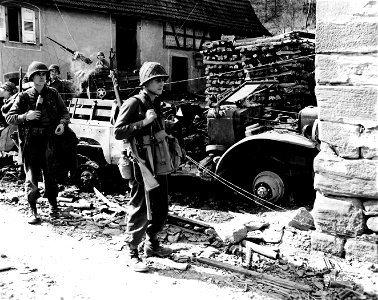 SC 396876 - Two weary 7th U.S. Army men halt for a break by burnt out weapons carrier in Reipertswiller, during 42nd Infantry Division push through Domaniale Forest. 16 March, 1945.