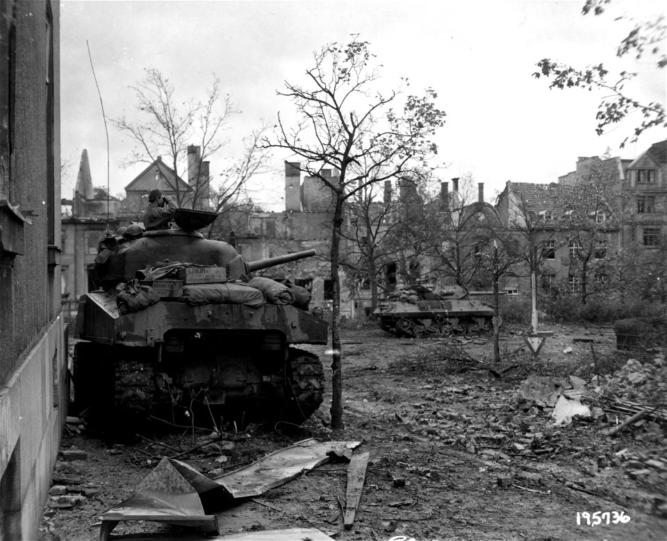 SC 195736 - From the turret of a medium tank, Cpl. Eugene McKay, Calumet City, Ill., searches for Germans in Aachen, Germany, while a tank destroyer, in the background, moves on German positions. 20 October, 1944.
