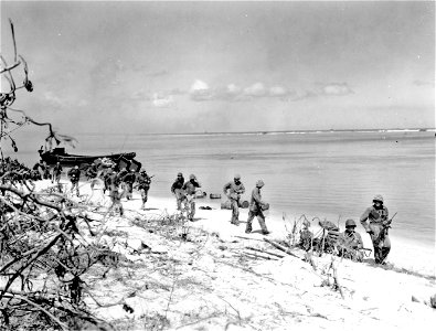 Marine infantrymen on the double, move along Saipan beach to take up new positions.