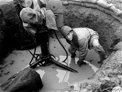 SC 329688 - Pfc. George Denmeade Jr., of Struthers, Ohio, uses an old ration can in an attempt to bail out the pit which conceals his machine guns. 17 November, 1943. photo