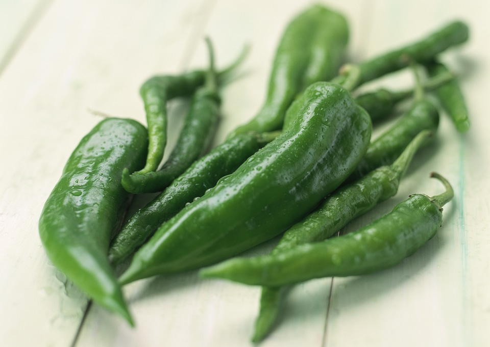Long green chili peppers resting on wooden board surface