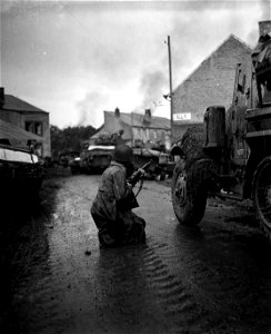 SC 364275 - Pfc. Lowell Holt, West Des Moines, Iowa, a member of the 5th Armored Division, takes cover behind a truck as he gets set to draw a bead on a German sniper across the street.