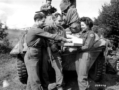 SC 329774 - Miss Helen Rehak, St. Louis, Mo., an American Red Cross Clubmobile girl, passes out cigarettes to members of an American reconnaissance unit who have halted their motorized vehicle near the Moselle River, France. 8 September, 1944. photo