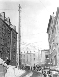 SC 329982 - Old and new communications lines are webbed across street at a road intersection in Bastogne, Belgium. 20 January, 1945.