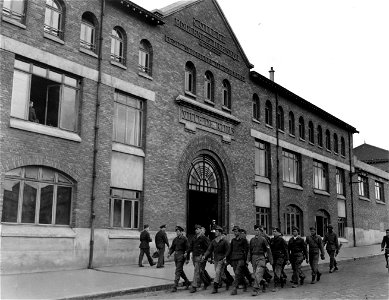 SC 374878 - Captured German troops march past the main entrance to the "little red schoolhouse", SHAEF HQ on Rue Henry Joliaeur, in Reims, France, where German officers signed the unconditional surrender terms formally ending the war in Europe.