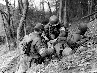 SC 198841 - Pfc. Charles Naughty, Long Island, N.Y., and Pfc. Thomas West, American Fort, Utah, both medics of Company I, 3rd Battalion, 8th Regiment, 4th Infantry Division, treat a wounded infantryman in the Hurtgen Forest. photo