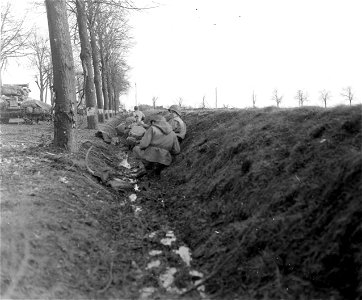 SC 270821 - American infantrymen lie in a roadside ditch, seeking shelter from enemy shellfire, awaiting orders to advance on the town of Obergeich, Germany.