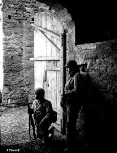SC 270669 - Two infantrymen of the 4th Division, U.S. Third Army, near Prum, Germany, stay concealed behind a barn door as they await orders to push on to the next objective. photo