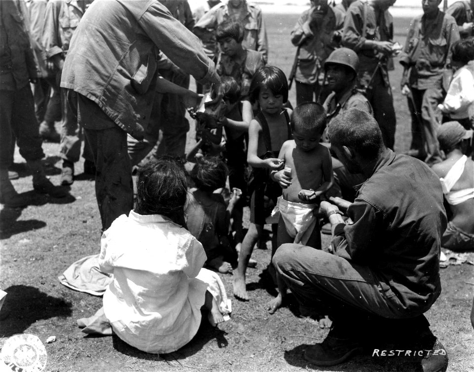 SC 405065 - American soldiers pass out K rations to native children. Small Japanese boy in foreground seems happy with his share.