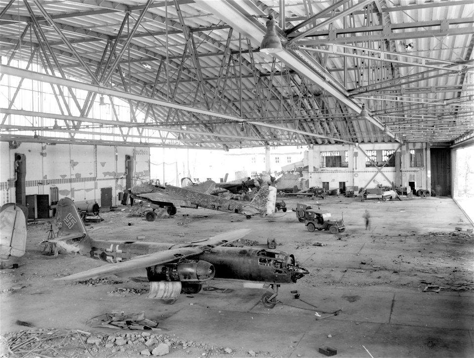 SC 195630 - German twin-engined, jet-propelled fighter plane, in foreground, and other planes were abandoned by Luftwaffe troops in large hanger of German airfield captured by III Corps, 3rd U.S. Army, at Manching, Germany.