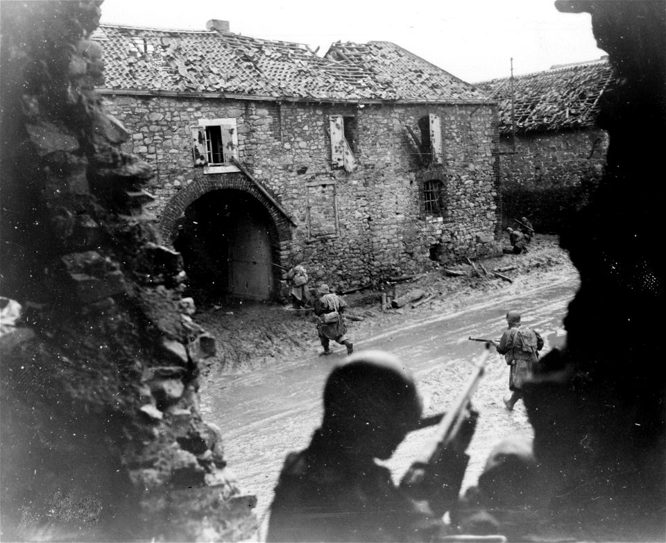 SC 270808 - American soldier with B.A.R. silhouetted between shattered walls of building in foreground covers riflemen dashing across street of battle-scarred German village near the frontlines during realistic battle practice.