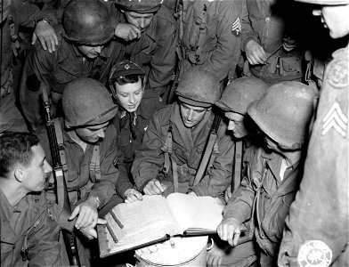 SC 329776 - Miss Peggy Maslin, Port Chester, N.Y., a Red Cross worker in France, shows a bunch of GIs her clubmobile autograph book, while Pvt. Wm. Putnam, Pittsfield, Mass., adds another name to it. 1 October, 1944.