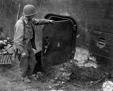 SC 336769 - Pvt. Lawrence J. Lewis, of Chetek, Wis., examines the effect of a shell near the entrance to a German pillbox that formed part of the Siegfried Line defenses on the Dutch-German border.