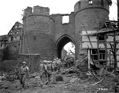 SC 270831 - Troops of the 9th Infantry Division, U.S. First Army, file through the wreckage and an archway in the town of Nideggen, Germany. 28 February, 1945. photo