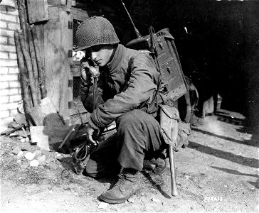 SC 195513 - Pfc. Archie Torten "gets the message thru" with a walkie-talkie which he operates from the side of a house on the outskirts of a French town.