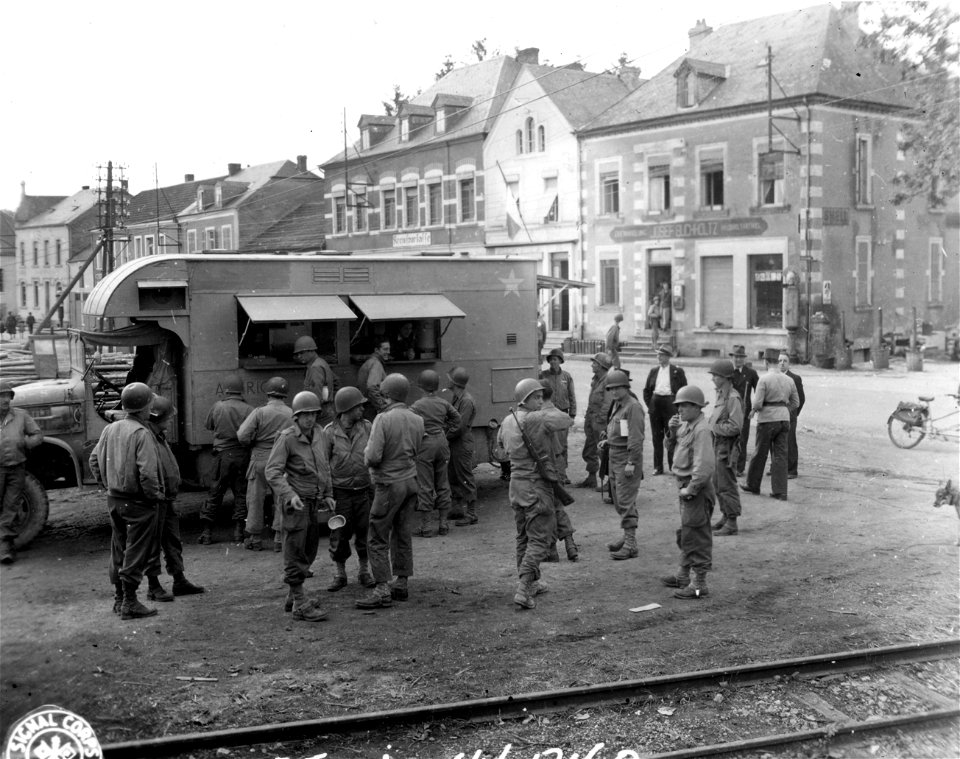 SC 329730 - Infantrymen take break in fighting to enjoy coffee and doughnuts offered by Red Cross girls of Clubmobile "General Lee" somewhere in Luxembourg. 9 October, 1944.