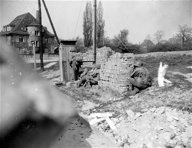 SC 270643 - Seventh Army riflemen take cover from heavy machine gun fire behind shed at street corner in bitterly-defended Nurnberg, famous Nazi shrine and German industrial center.