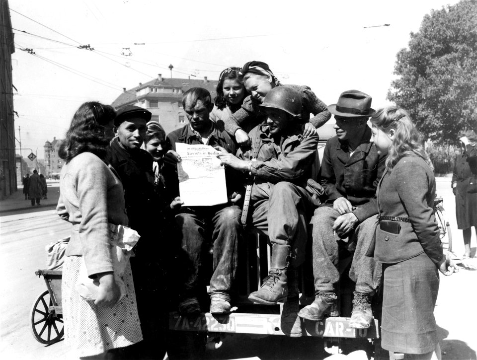 SC 405036 - Pvt. Troy Patrick, Salyersville, Ky., takes time out to show some liberated Russians the news of the "Soviets in Berlin" in a copy of the Stars and Stripes.