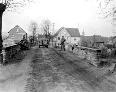 SC 335285 - 1st U.S. Army soldiers stand guard as American vehicles pass over Katzenfurt Bridge over the Dill River, Germany. The bridge was left intact by the fleeing enemy. 27 March, 1945.