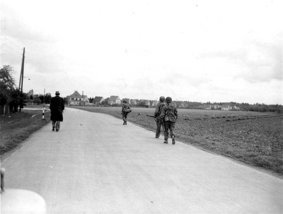 SC 270654 - The German civilian on the left of the road walks into the city with three infantrymen, giving directions and what information he can. 30 April, 1945.