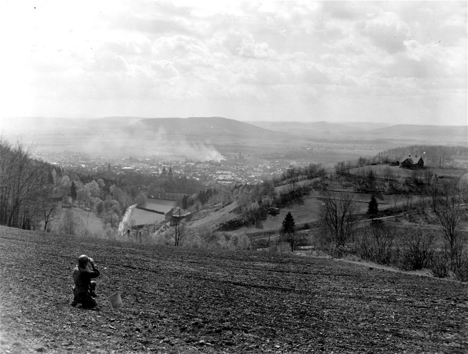 SC 336822 - T/4 Warren J. Rothenberger, 39th Signal Company, 26th Infantry Division, surveys the burning heart of Sonnenburg, Germany, shortly after troops of the 26th "Yankee" Division stormed into the town.