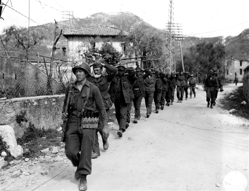 SC 337146 - Sam Yoshihana, Chicago, Ill., leads a bunch of German prisoners taken by the 100th Bn., through the village of Valecchia to a PW cage. 8 April, 1945.