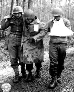 SC 196225-S - An unwounded GI, left, and one that has been slightly wounded, right, help a third man to a jeep that will take him to a hospital in the rear area. photo