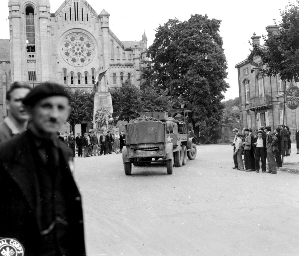 French civilians gather to watch the American trucks pass through the town square in Bar-le-Duc, France. Note the French and Russian flags flying from the World War I monument. 1 September, 1944.