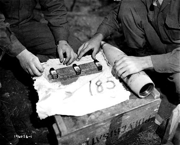 SC 196056-S - D-ration chocolate bars and bottles of Halazone pills are packed into 105mm howitzer shells to be fired to men in an Infantry battalion that is cut off by Germans in the Belmont sector, France. 29 October, 1944.