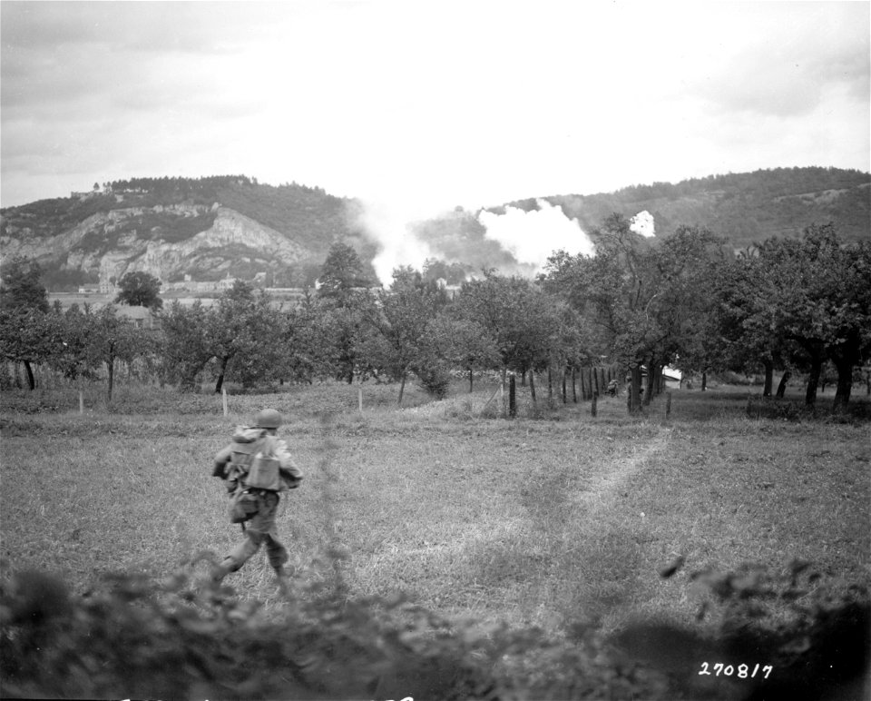 SC 270817 - In the advance across the Meuse River in Belgium, this U.S. infantryman races for cover of trees ahead. The river lies a few hundred yards ahead of this point.