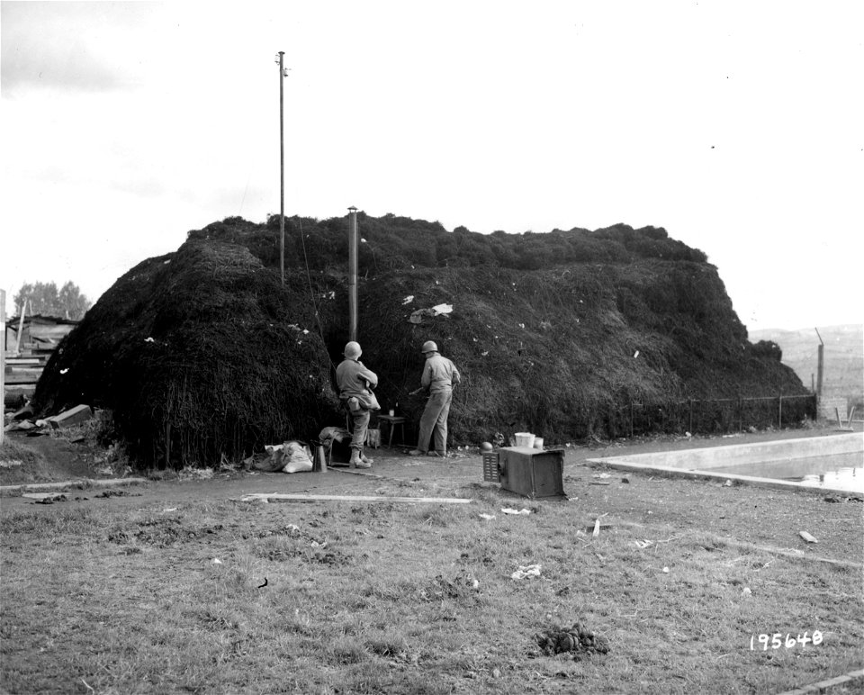SC 195648 - With carbines cocked, two U.S. infantrymen cautiously enter a Nazi pillbox near a factory in Aachen, Germany, which German soldiers had disguised as a scrap heap by covering it with scrap metal. 13 October, 1944.